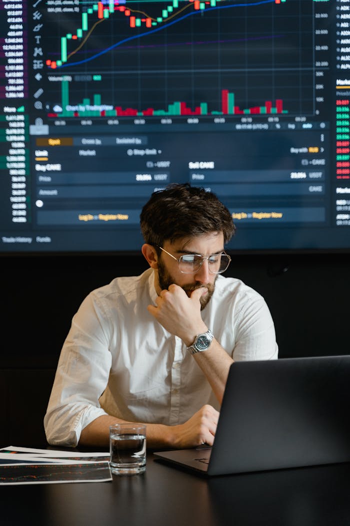 services-03 Pensive businessman with a beard analyzing stock market trends on a laptop in an office setting.